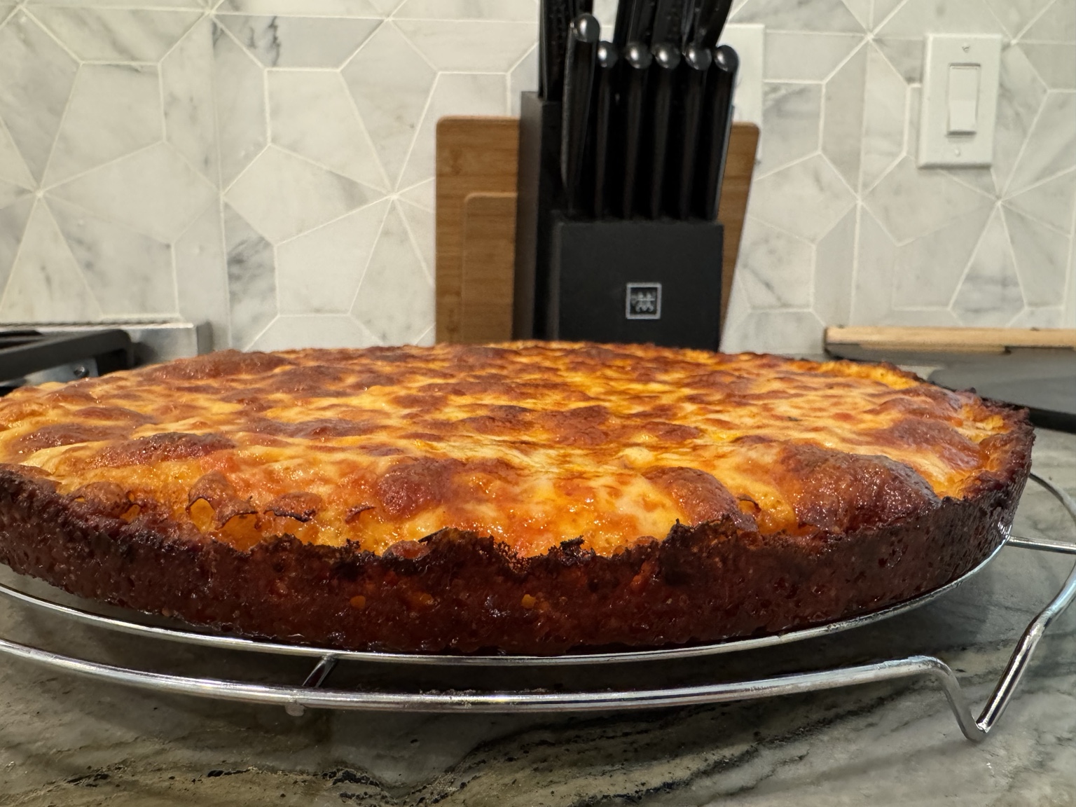 Greg’s round pan pizza with a browned cheese edge, cooling on a rack.